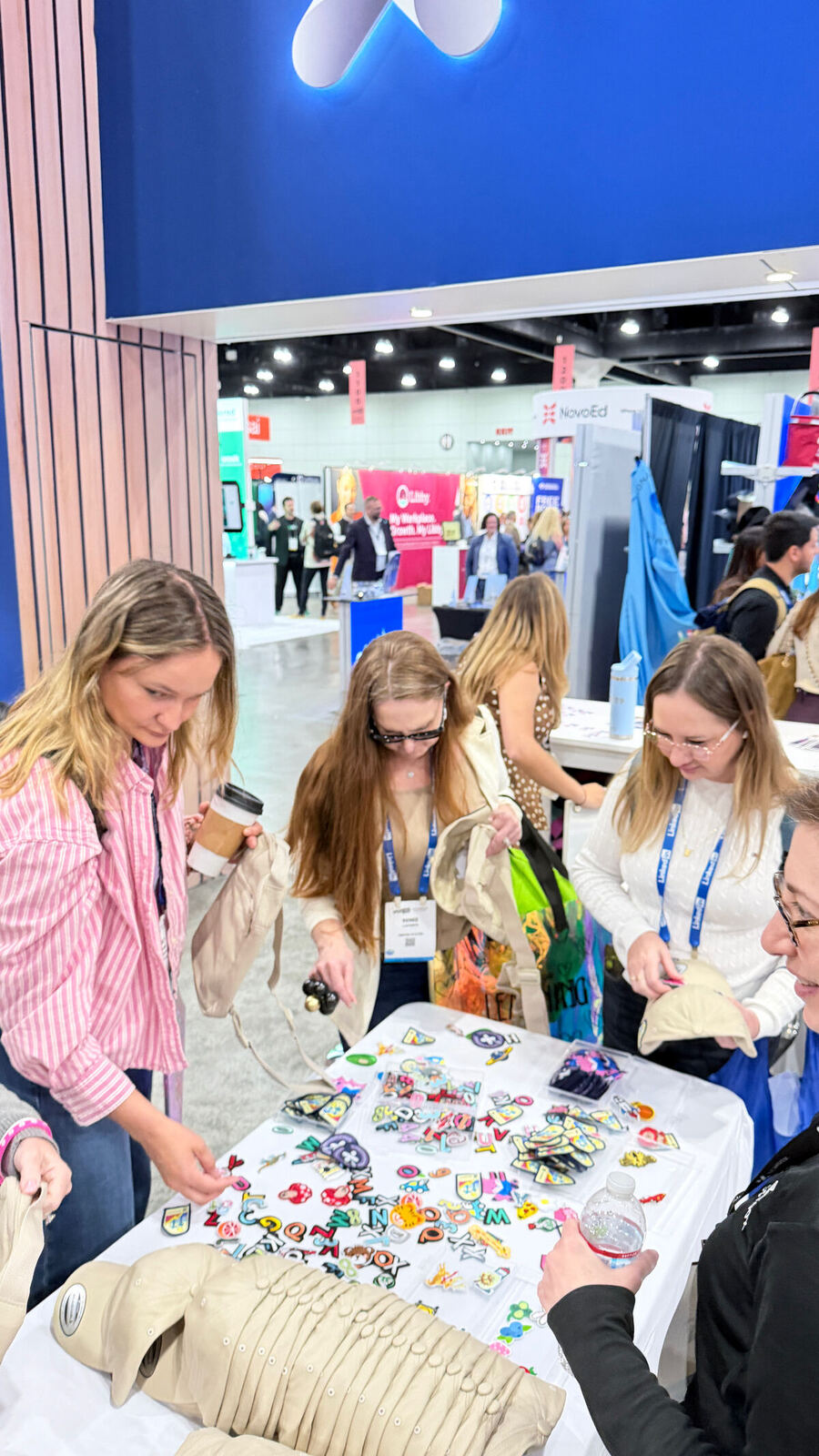 Convention attendees picking colorful chenille letters from trays at a trade-show booth table